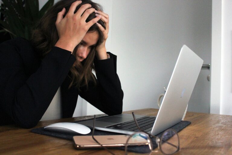 Mujer frustrada con las manos en la cabeza frente a una laptop, simbolizando problemas con redes sociales o tecnología.