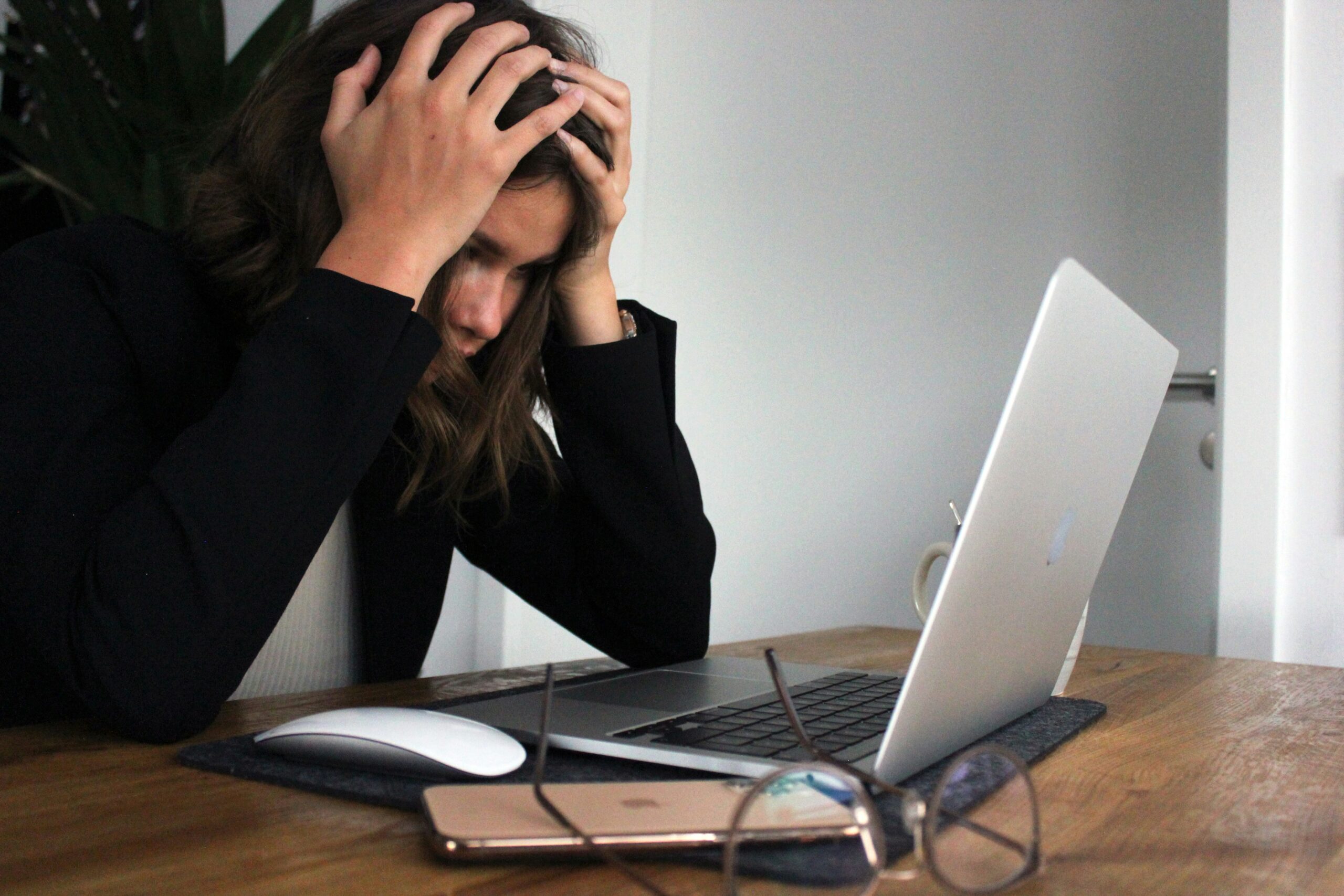 Mujer frustrada con las manos en la cabeza frente a una laptop, simbolizando problemas con redes sociales o tecnología.